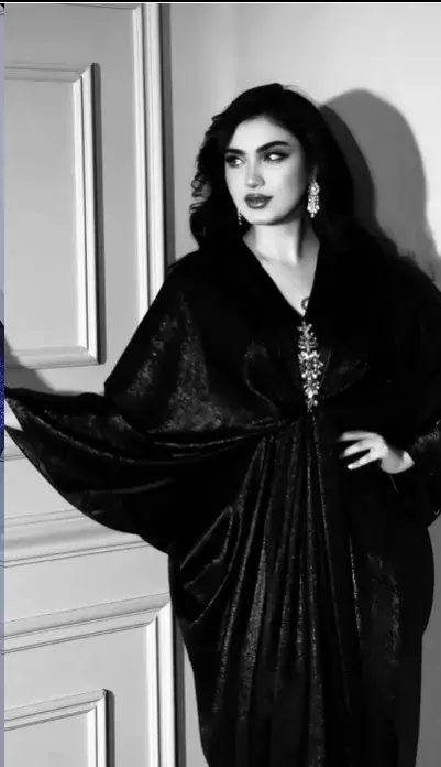 Model in a black velvet kaftan with batwing sleeves and a jewelled clasp, black and white