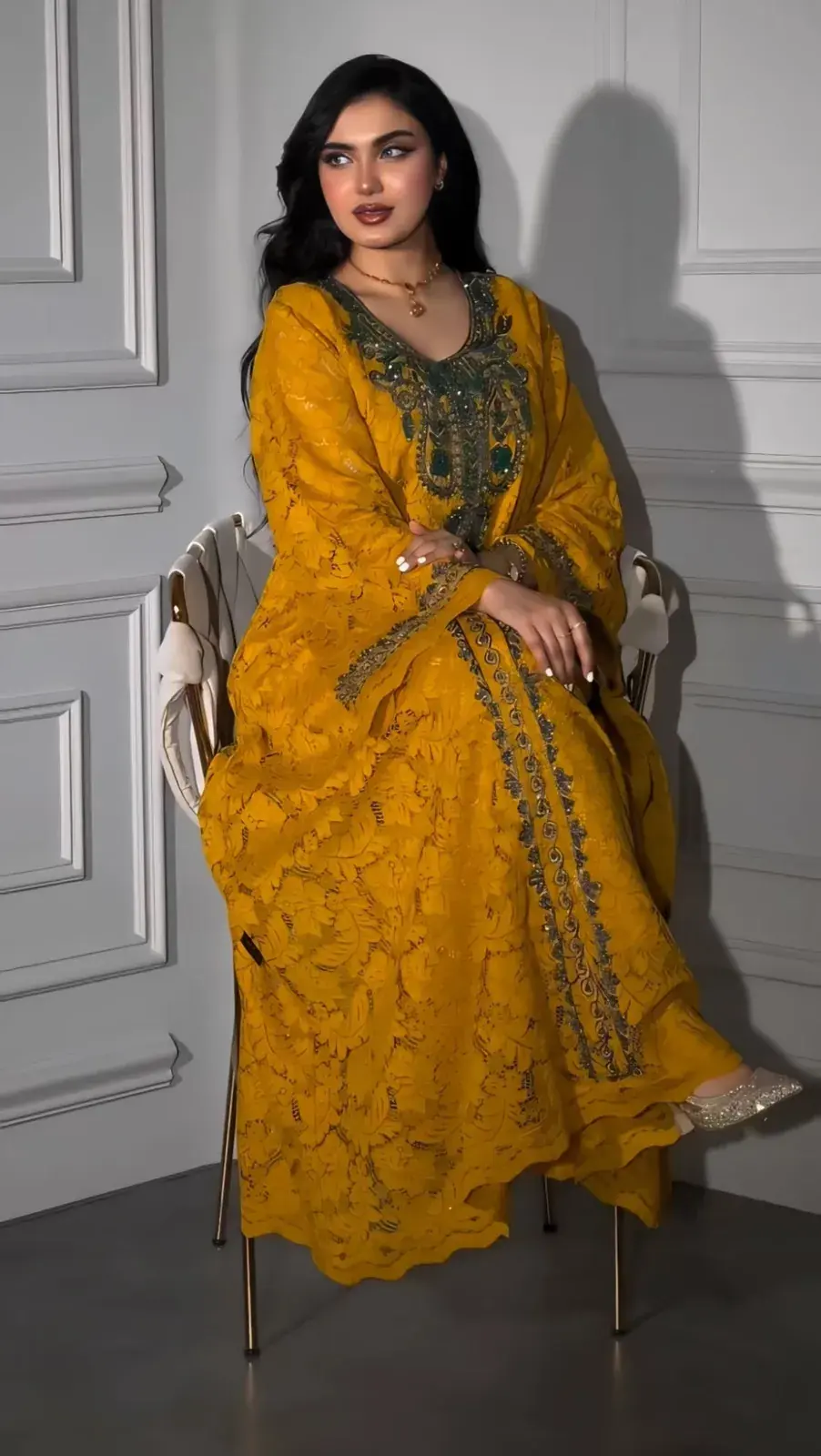 Model seated in a saffron kaftan with tonal floral embroidery and a green embroidered neckline