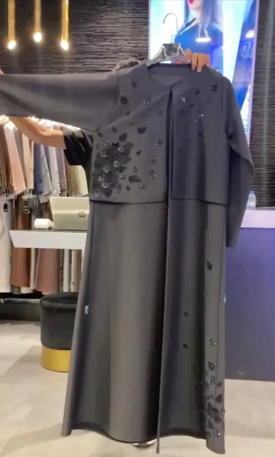 Graphite abaya with black leaf appliqué on the bodice and hem, shown on a hanger