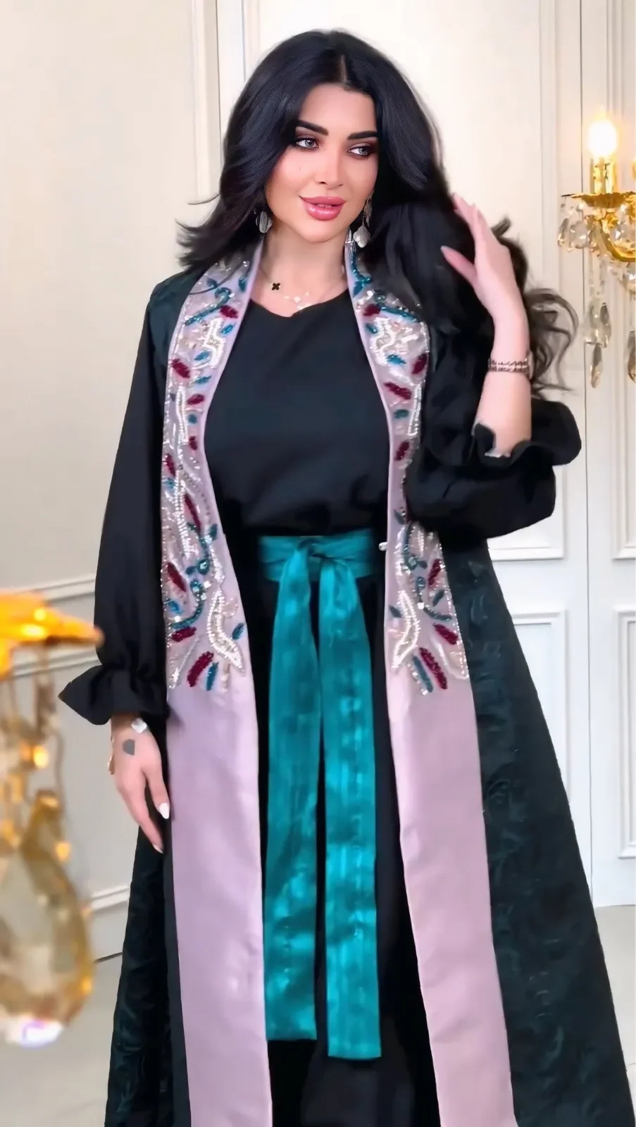 Model in a black abaya with blush-lined embroidered lapels and a teal sash