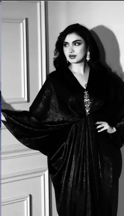 Model in a black velvet kaftan with batwing sleeves and a jewelled clasp, black and white