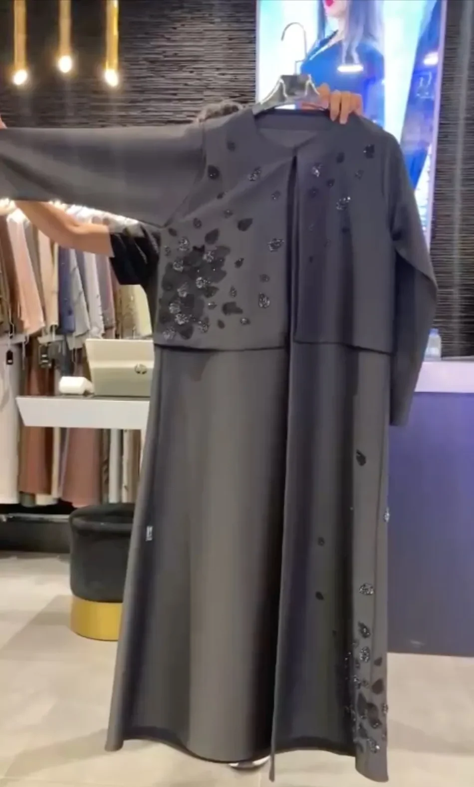 Graphite abaya with black leaf appliqué on the bodice and hem, shown on a hanger