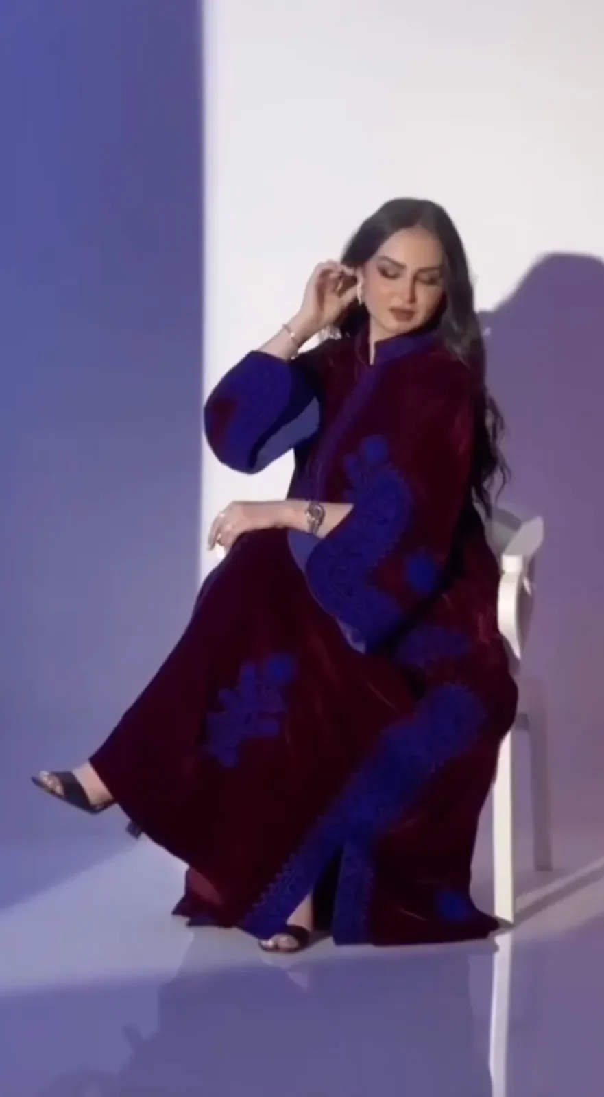Model seated in a plum velvet jalabiya with blue embroidery on the sleeves