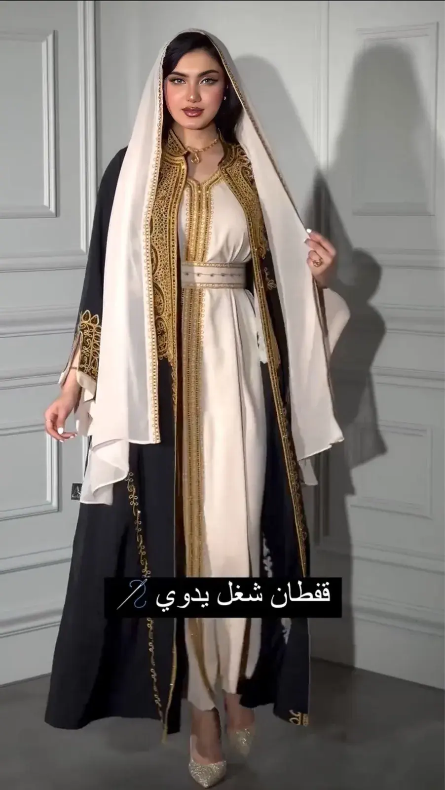 Model in an ivory kaftan with gold hand embroidery under a black open abaya, with an ivory shawl
